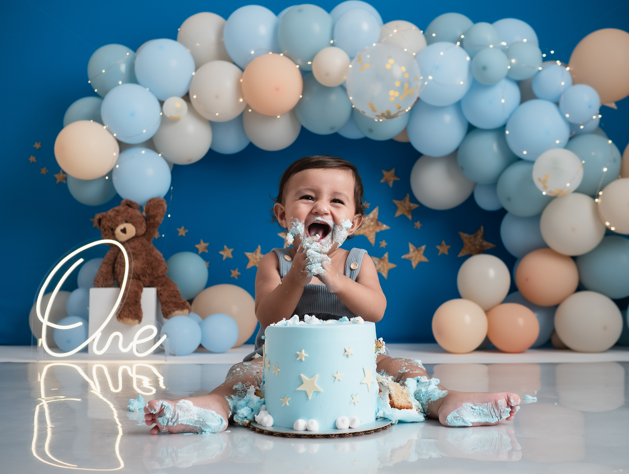 Bebé sonriendo frente a su pastel en una sesión Cake Smash azul con estrellas
